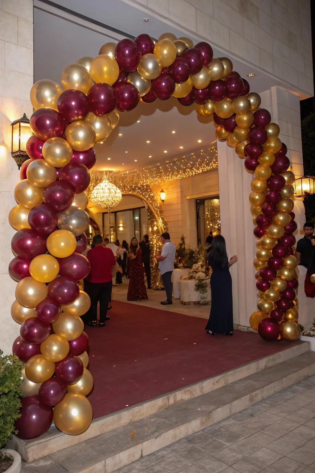A stunning decorative balloon arch in deep red and gold warmly welcomes guests with flair.