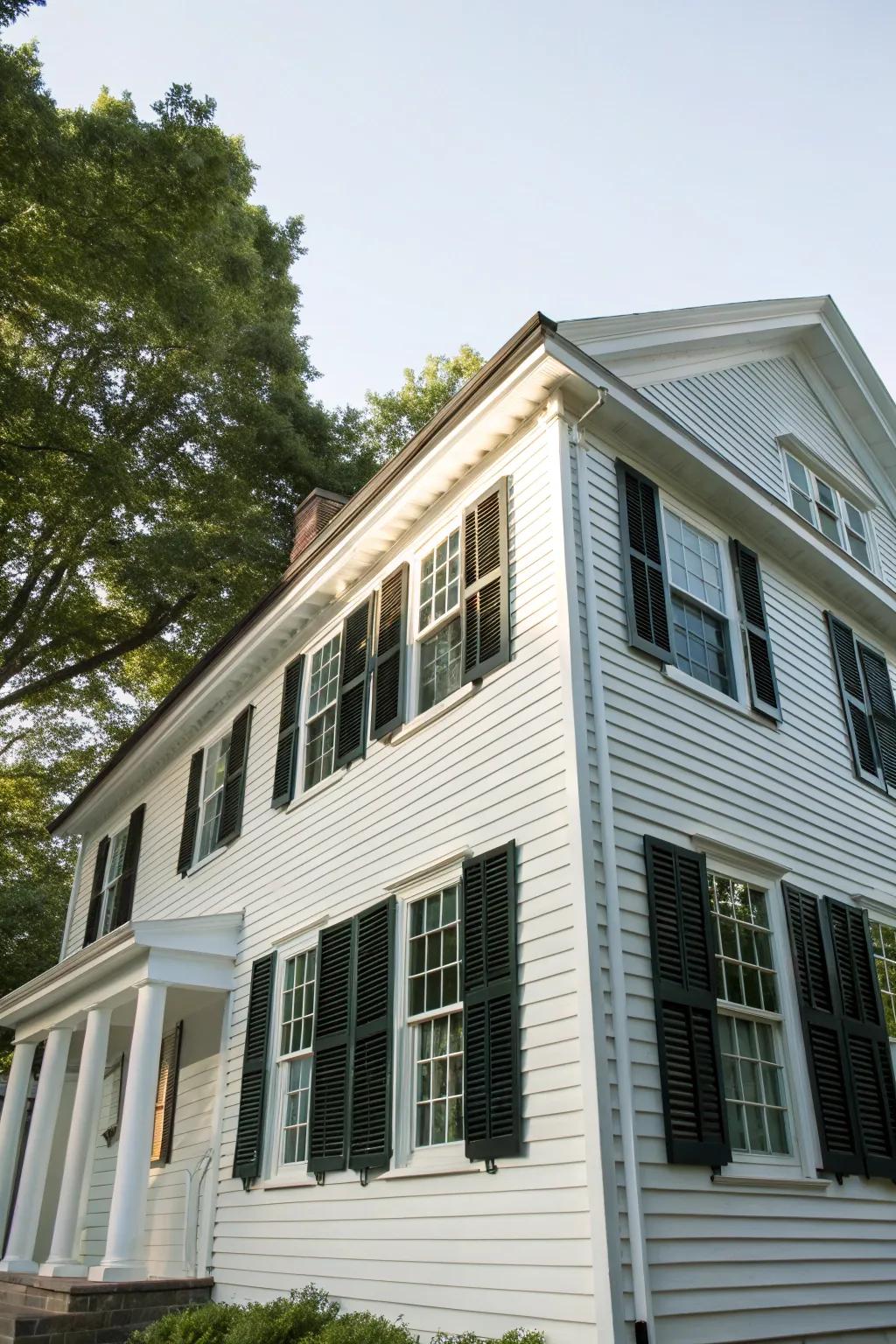 A colonial-style house showcasing traditional white panelling and contrasting dark window coverings.
