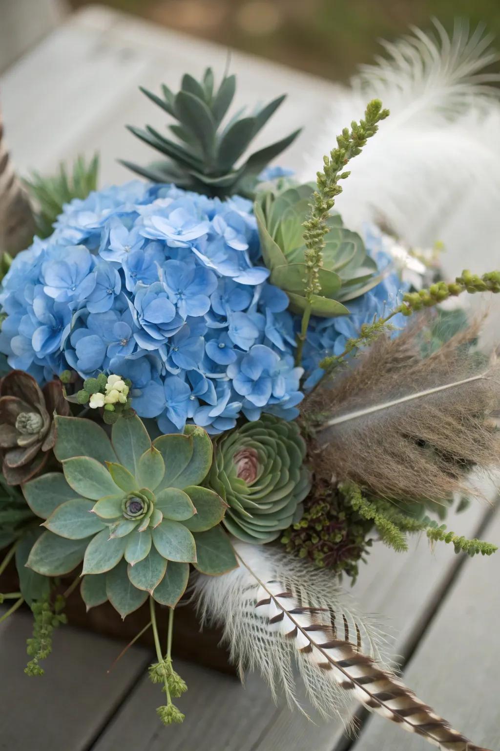 An eclectic centerpiece with blue hydrangeas, succulents, and feathers.