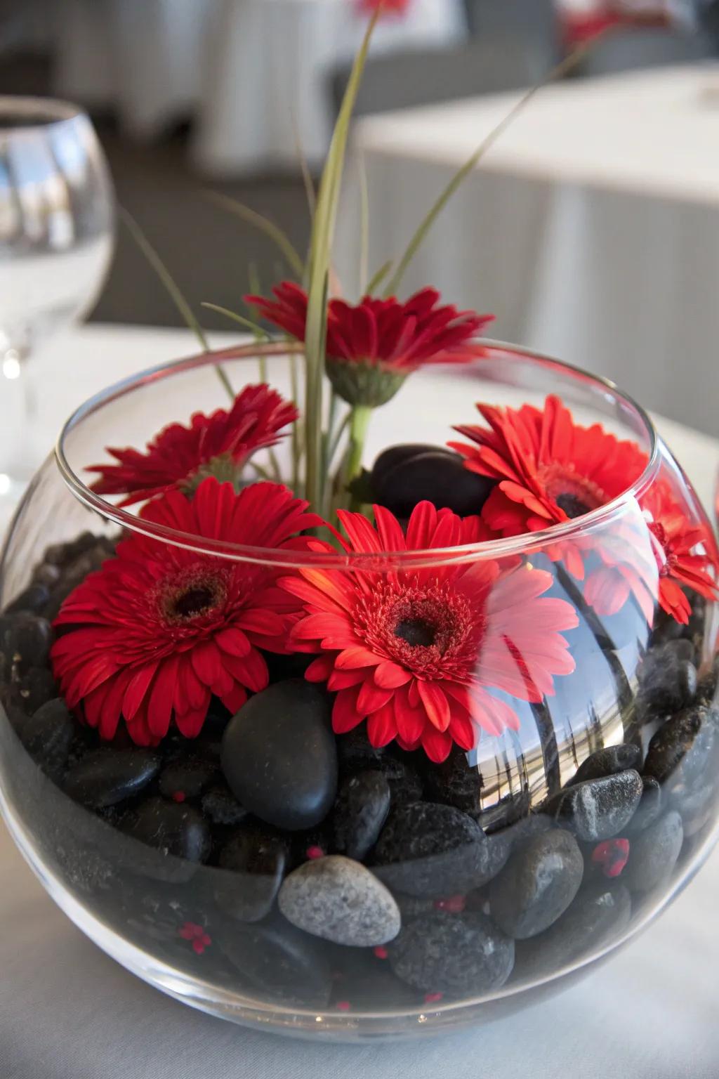 Scarlet flowers drifting over charcoal pebbles layered in a glass container for a serene display.