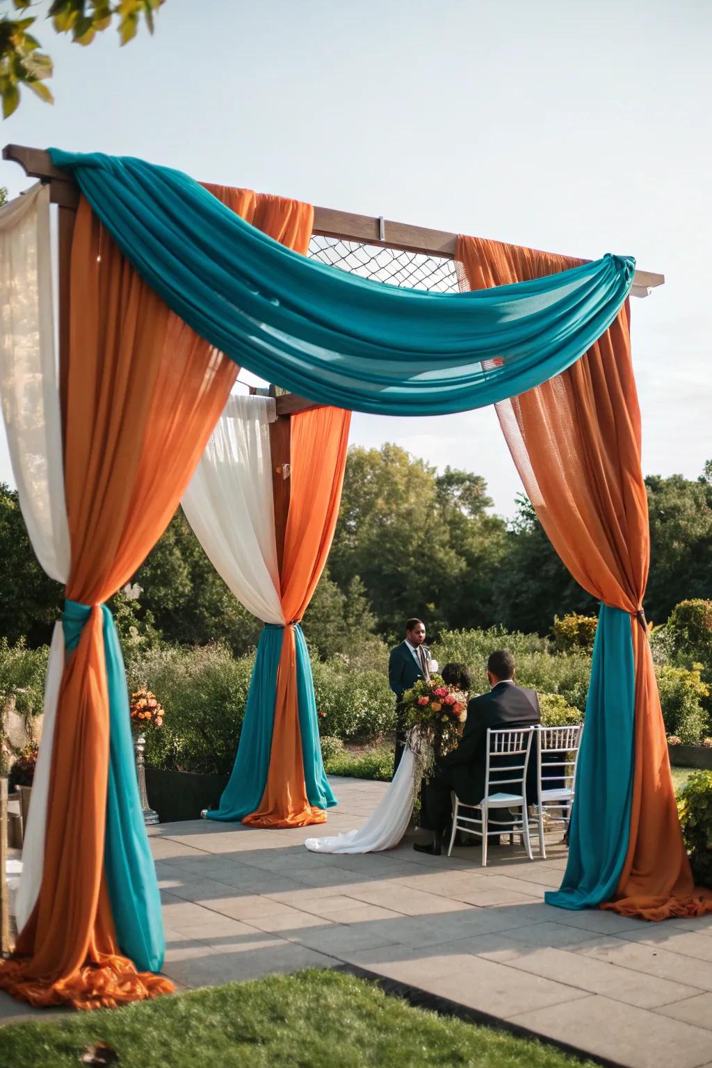 A ceremony arch draped in gorgeous seafoam green and sunset orange fabrics.